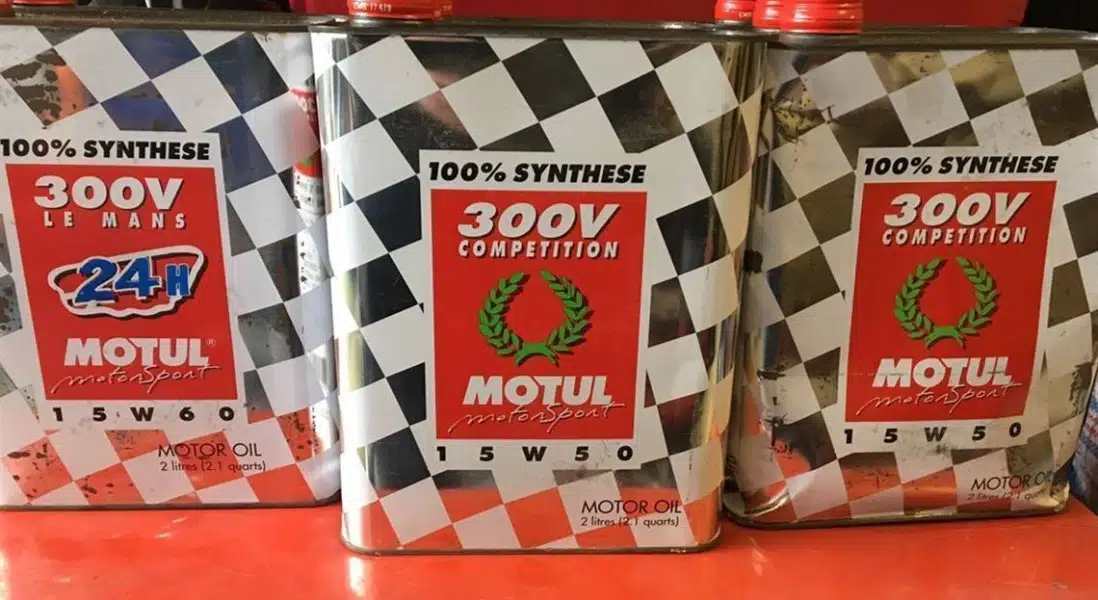 Три жестяные банки моторного масла Motul 300V с гоночным дизайном в клетку и надписью 100% Synthese.