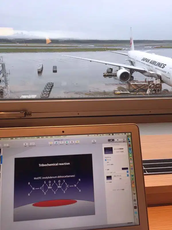 Ноутбук с презентацией трибохимии на фоне самолета Japan Airlines в дождливом аэропорту.