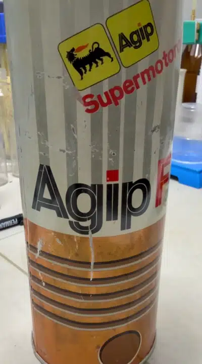На фото металлическая банка моторного масла Agip Supermotoroil с логотипом черного пса с языком пламени.