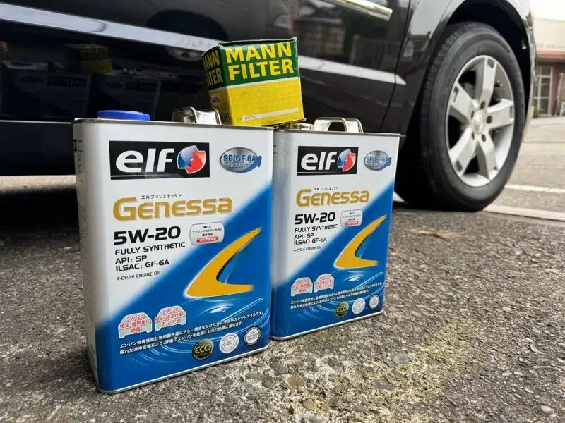 На фоне автомобиля канистры с моторным маслом Elf Genessa 5W-20 и масляный фильтр Mann Filter.