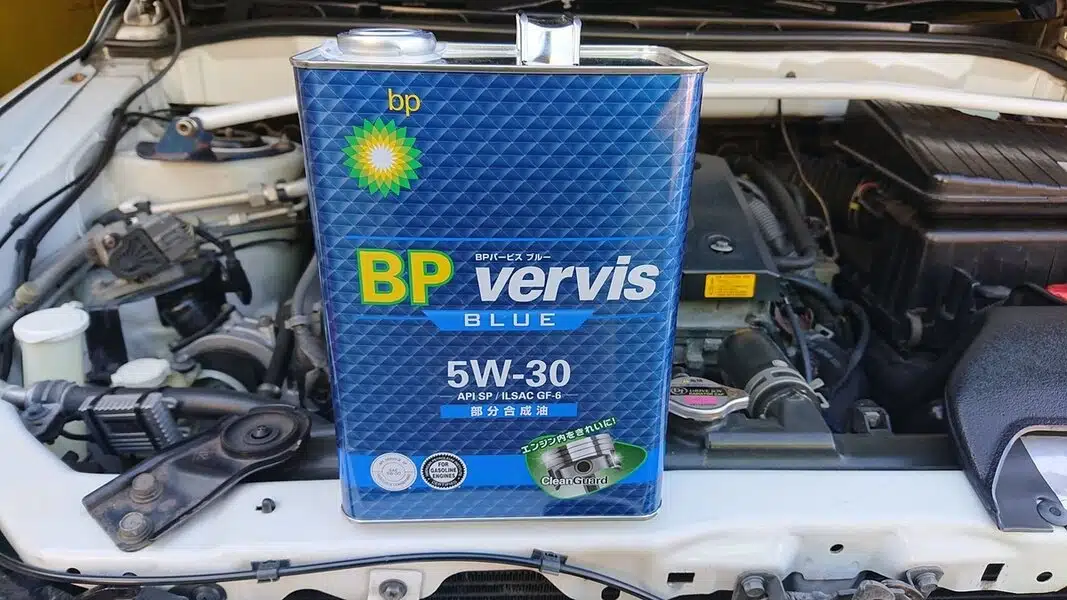 Канистра моторного масла BP Vervis Blue 5W-30 на фоне автомобильного двигателя.