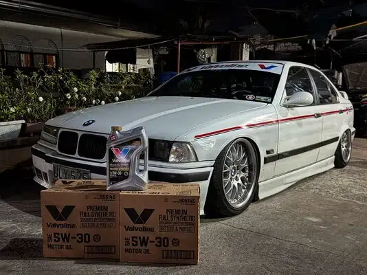 Белый BMW с маслом Valvoline на фоне ночного городского пейзажа.