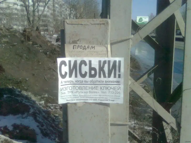 На столбе объявление с крупной надписью Сиськи для привлечения внимания к изготовлению ключей.