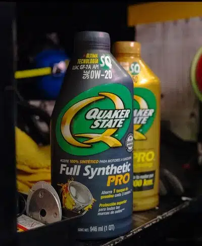 Две бутылки моторного масла Quaker State Full Synthetic PRO на полке в гараже.