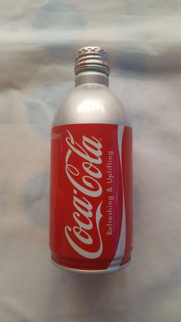 На фото банка Coca-Cola в серебристо красном дизайне с надписью Refreshing & Uplifting на светлом фоне.