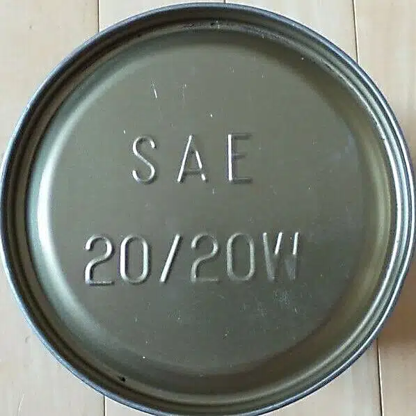 Крышка металлической банки с маркировкой SAE 20/20W на фоне деревянной поверхности.