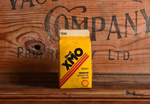 Желтая коробка Shell XMO с моторным маслом на фоне деревянной доски с надписью Company LTD.