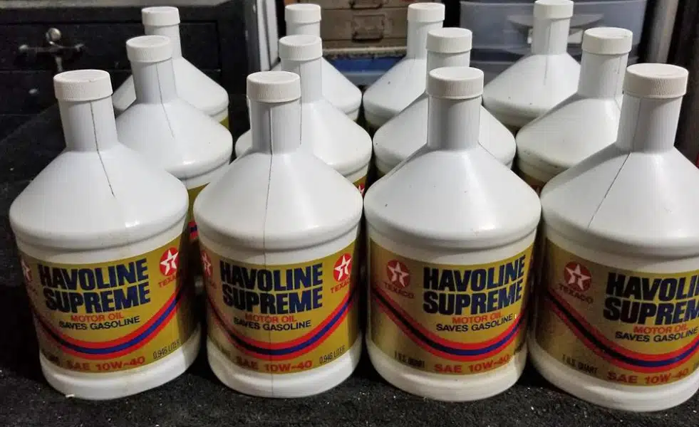 На фото много белых пластиковых бутылок с моторным маслом Havoline Supreme на фоне тёмной поверхности.