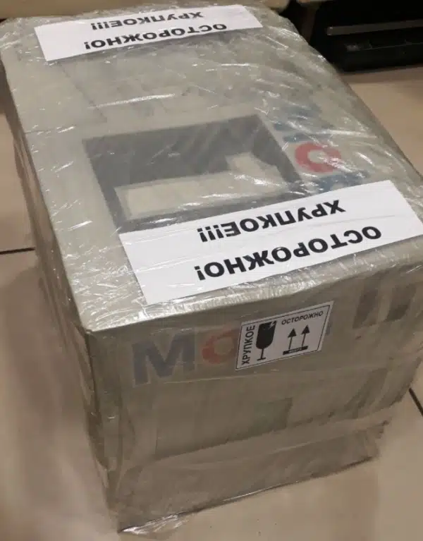 Плотная прозрачная пленка обволакивает серый ящик украшенный крупными надписями осторожно хрупкое гарантируя сохранность его содержимого при транспортировке.