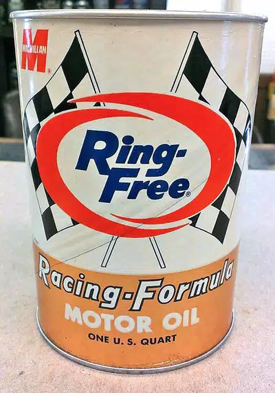Металлическая банка Macmillan Ring Free Racing Formula масла украшена гоночными флагами и ярким красным овалом.