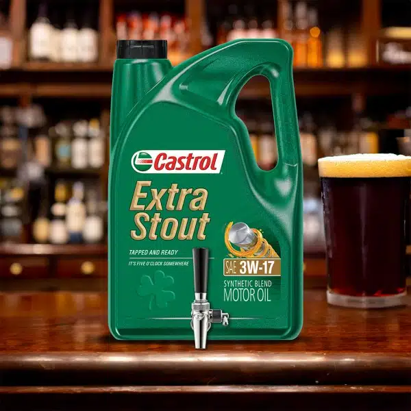Канистра масла Castrol Extra Stout с краном, рядом кружка пива на фоне барной стойки.