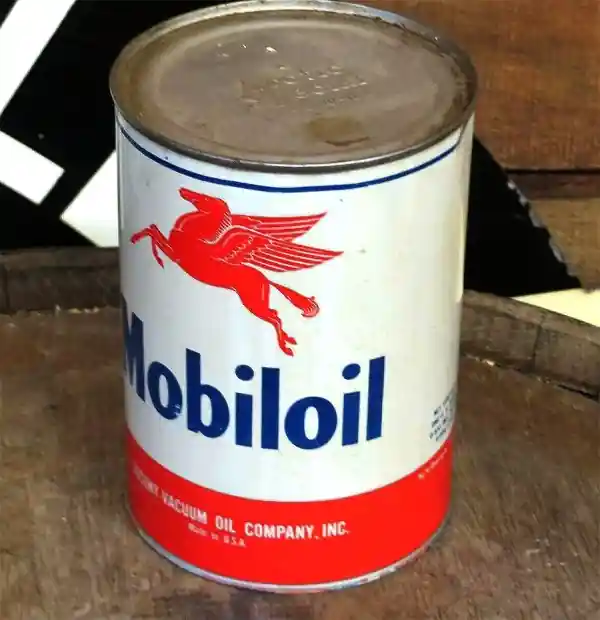 Винтажная банка моторного масла Mobiloil с красным пегасом на белом фоне стоит на деревянной поверхности.