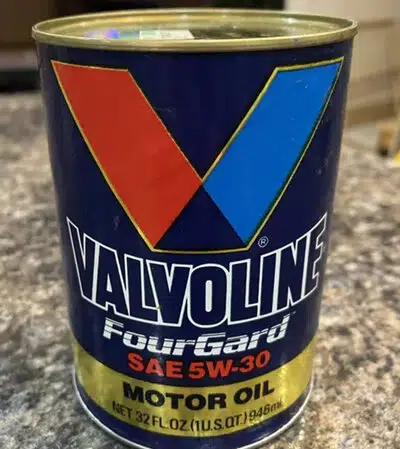 На фото синяя металлическая банка моторного масла Valvoline с красным и синим логотипом в виде буквы V.