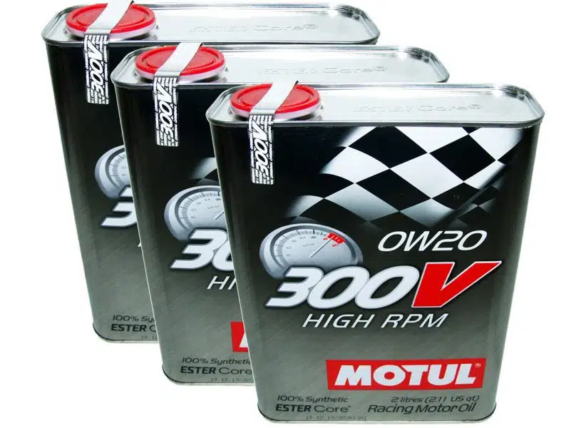 Три металлические канистры моторного масла Motul 300V с гоночной символикой и красными крышками на белом фоне.