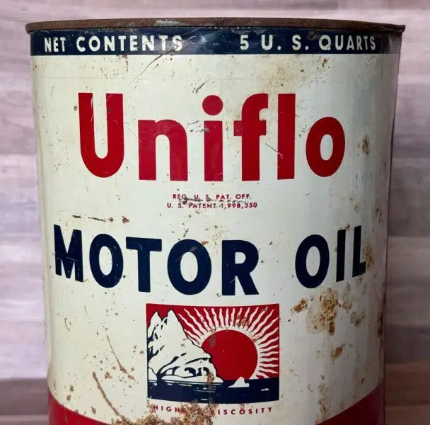 Винтажная банка моторного масла Uniflo с надписями красного и синего цвета и изображением солнца над горами на белом фоне.