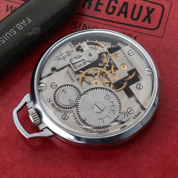 Открытый часовой механизм винтажных швейцарских часов Girard Perregaux с золотыми шестерёнками на красном фоне.