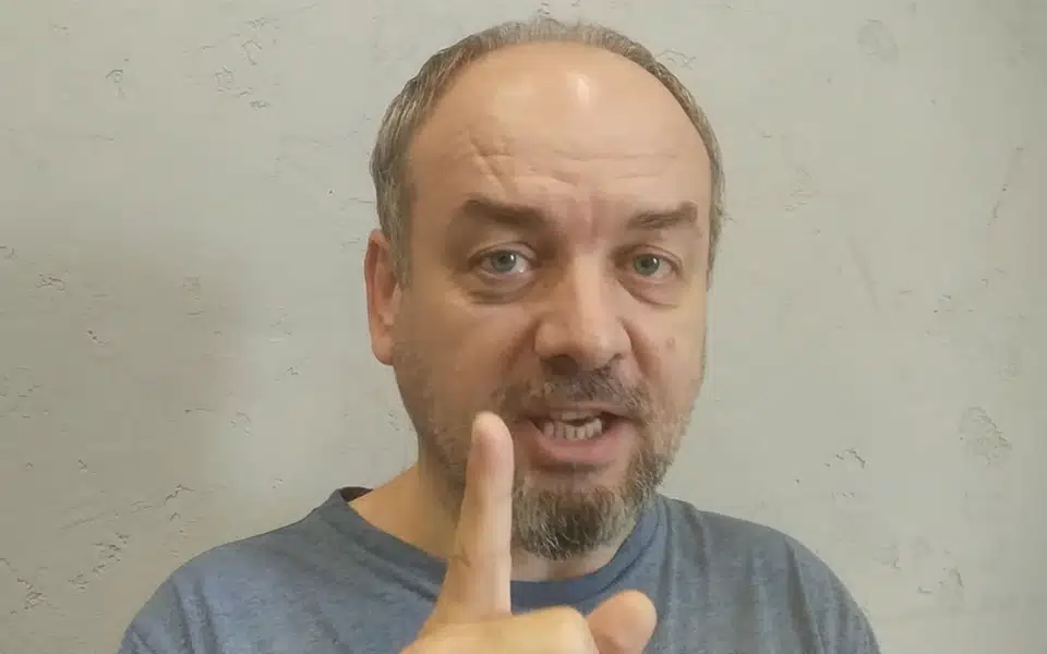 Мужчина с бородой показывает указательный палец вверх на сером фоне.