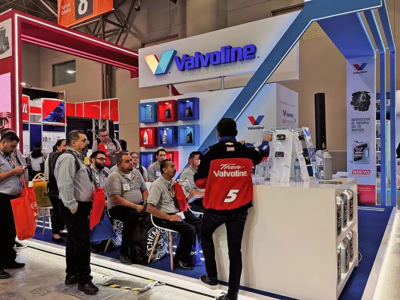 На выставочном стенде Valvoline посетители внимательно изучают представленную продукцию масел слушая пояснения специалиста.