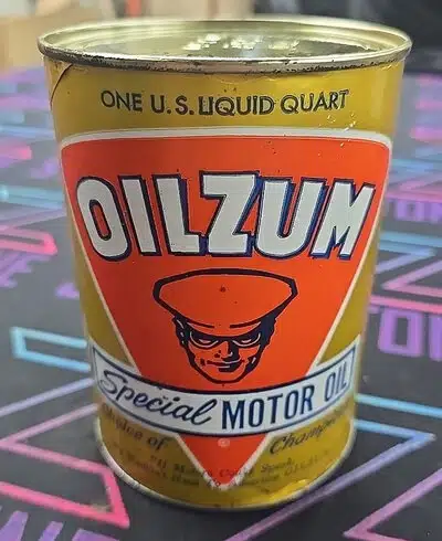 На картинке старая жестяная банка моторного масла Oilzum с ярким дизайном и изображением человека в фуражке.