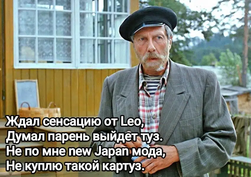 Портрет мужчины в стильном картузе пиджаке и тельняшке на фоне фрагмента деревянной архитектуры.