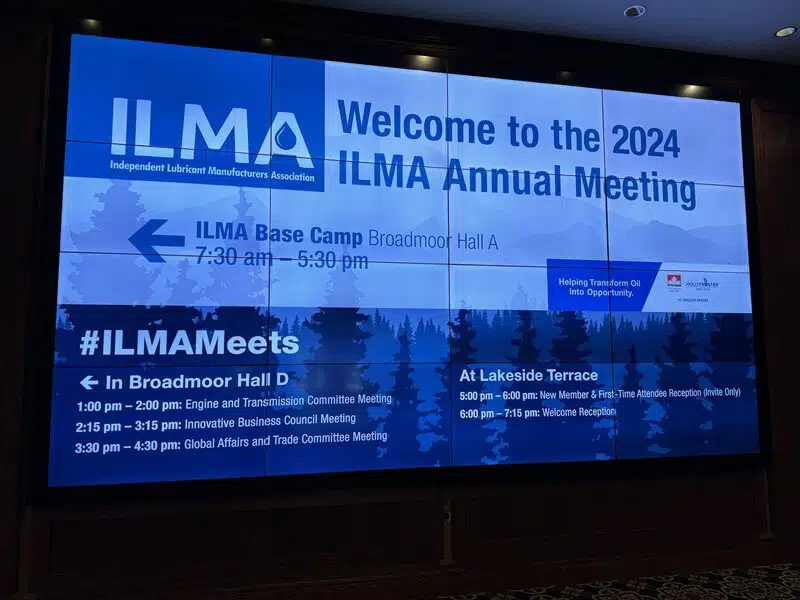 Большой экран с информацией о ежегодной встрече ILMA 2024, расписанием мероприятий и логотипами спонсоров на фоне стилизованного пейзажа.
